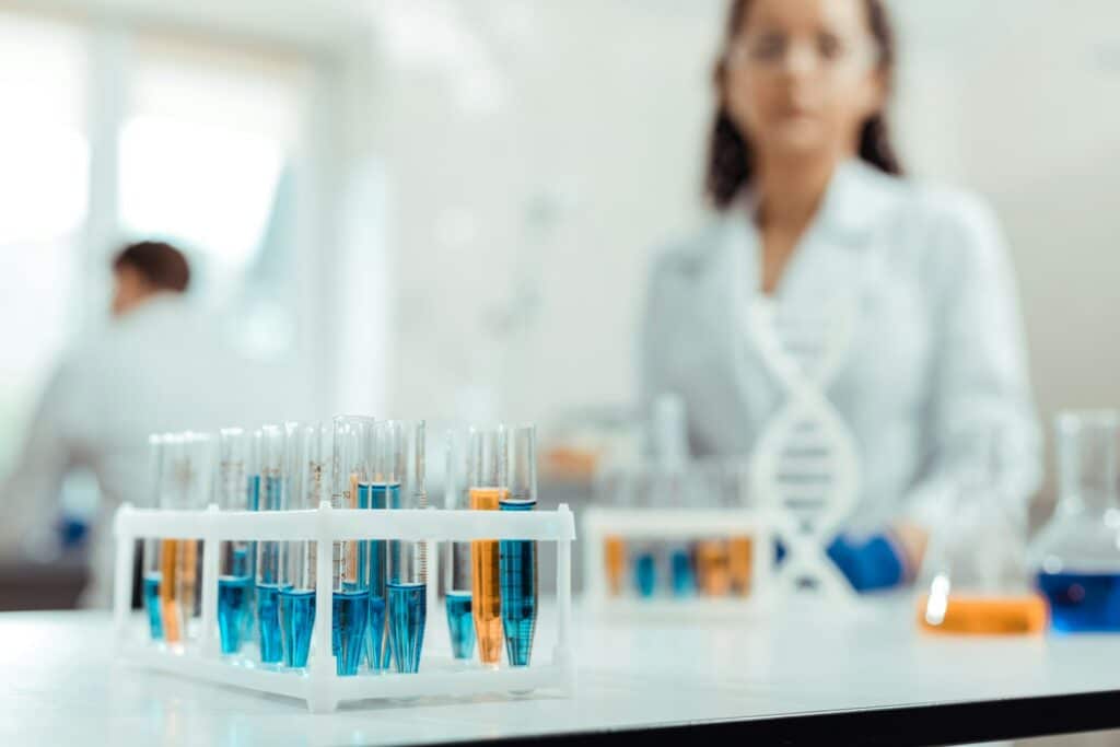 Close up of test tubes filled with coloured fluid with a lab tech in the background, representing wrongful dismissal in the Timmins v. Artisan Cells case